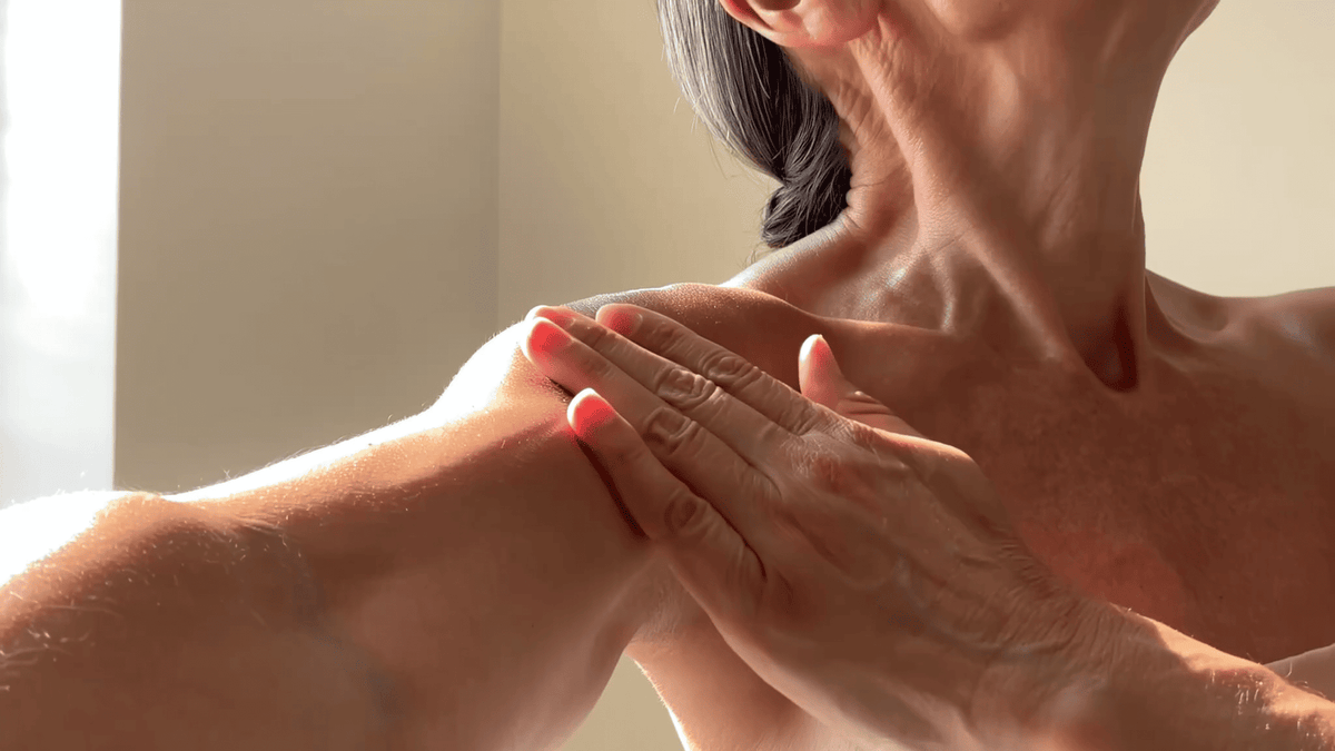 Woman smoothing body oil over her shoulder and arm in soft morning light
